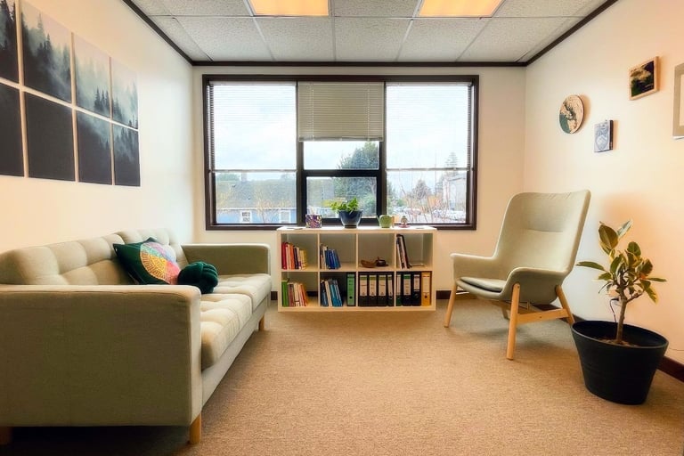 Inside view of the space with a couch, a bookcase and a chair in front of large windows