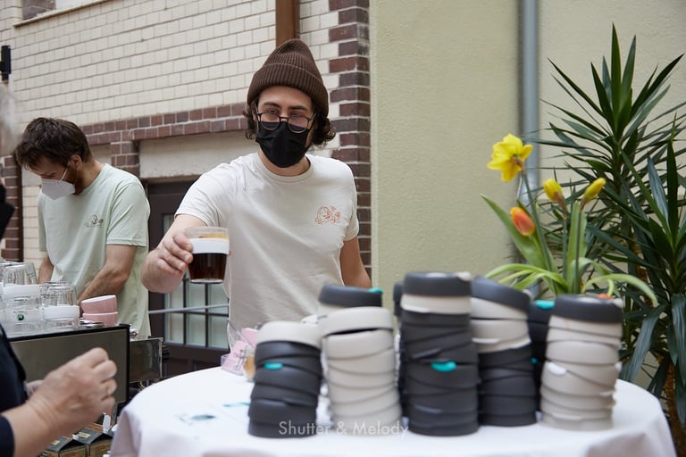 Ein Barista mit einer schwarzen Maske, der einen Kaffee serviert.