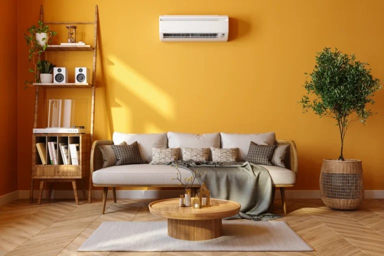 Modern wall-mounted air conditioner in a bright living room with yellow walls and a sofa.