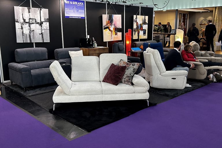 Modern white and grey sofas displayed on a purple carpet at a professional furniture trade show.