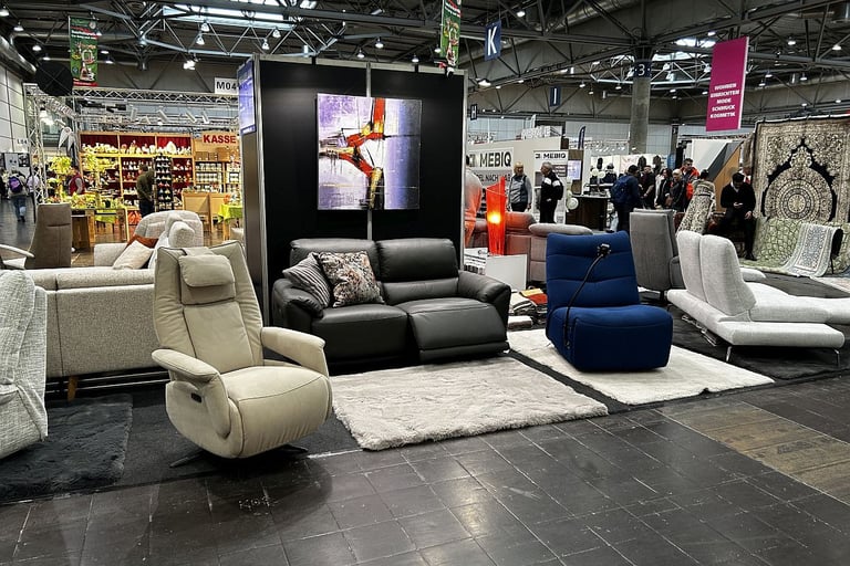 Modern living room furniture display at a trade fair featuring recliners, sofas, and area rugs.