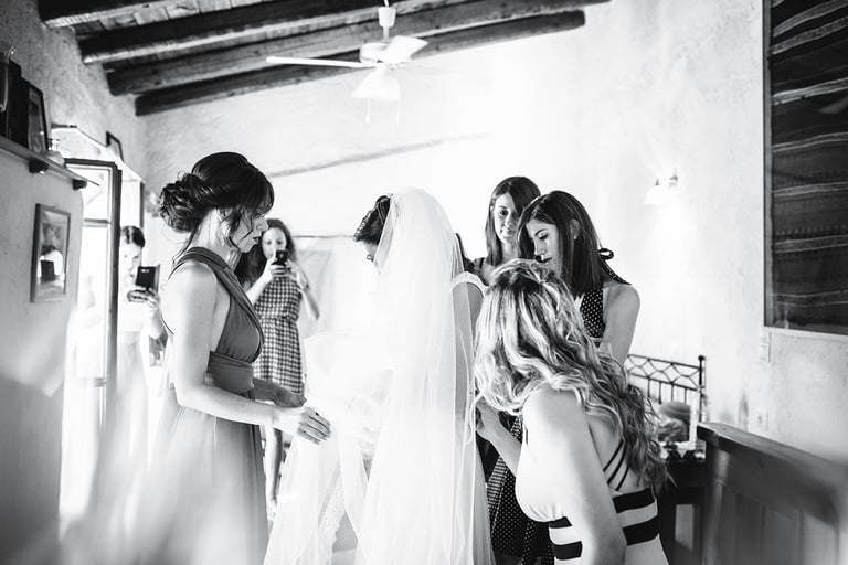 Fotografia in bianco e nero dei preparativi della sposa, mentre le amiche l'aiutano col velo dell'abito da sposa