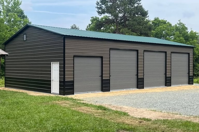 Large brown metal garage building with a green roof and four roll-up doors on a gravel pad.