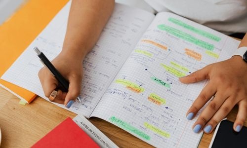 Student writing in a notebook with color-coded highlights for exam study and organization.