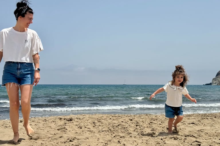 A mother and toddler daughter playing on a sandy beach by the ocean on a sunny day.