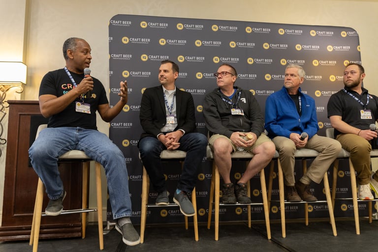 A panel of five craft beer professionals speaking at a conference event with a branded backdrop.