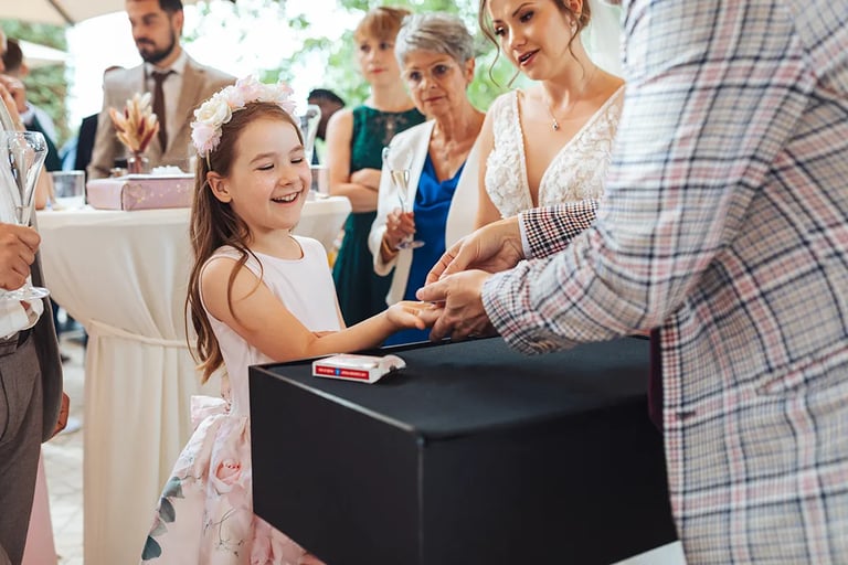 Enfant qui sourit devant un magicien lui faisant un tour de magie durant un mariage.