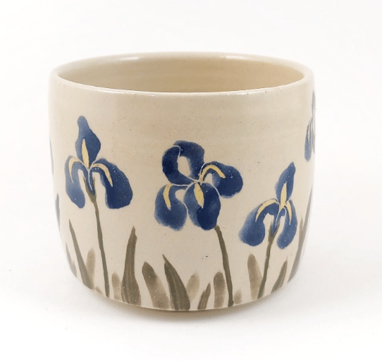 Handmade ceramic cup featuring hand-painted blue iris flowers on a cream glaze.