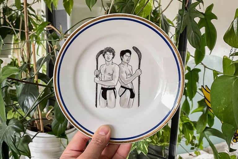 A decorative ceramic plate featuring an illustration of two shirtless hockey players surrounded by green houseplants.