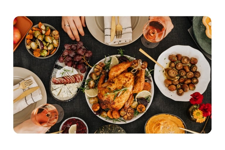 A festive holiday dinner table spread with roasted whole chicken, seasonal vegetables, wine, and appetizers.