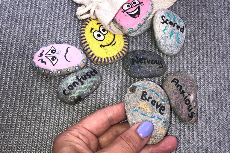 A selection of hand-painted therapy stones. One stone is being held, it says 'brave'. 