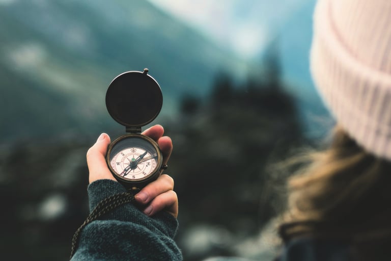 woman's hand holding compass in front of blurry nature backdrop