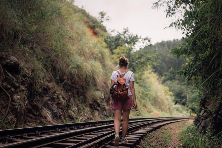 a woman walks along train tracks in a green pass