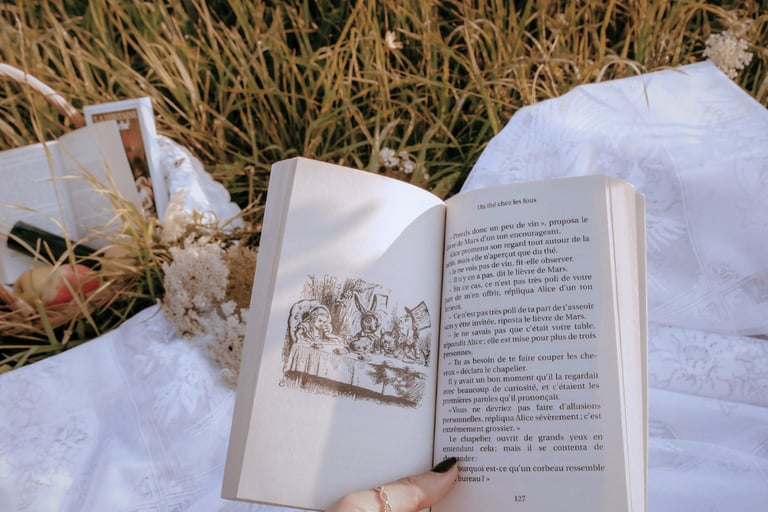 a hand holds a book over a field with wildflowers