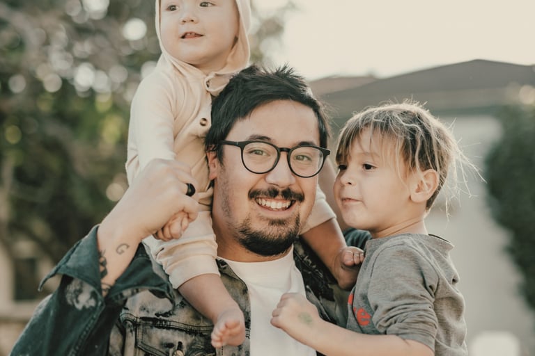 father smiles holding his two young children