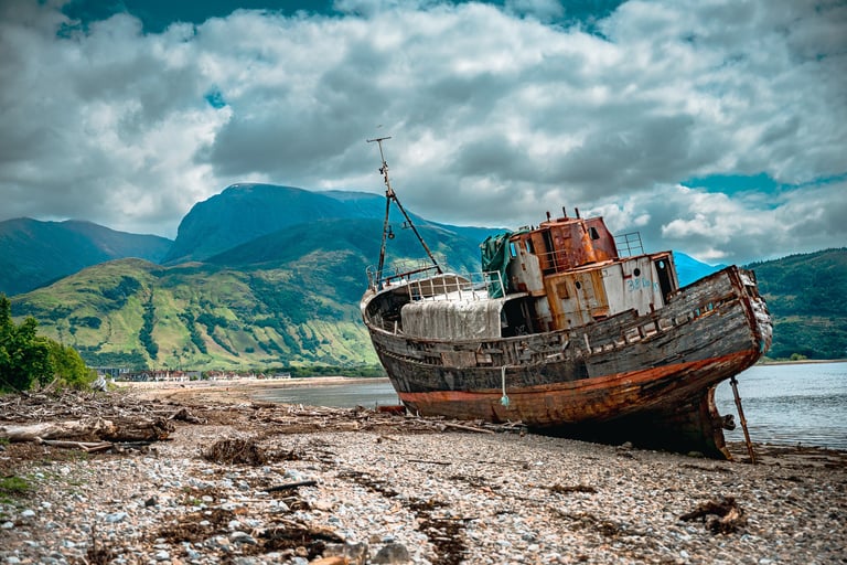 L’épave de Corpach repose sur la plage encadrée par les montagnes imposantes, créant une scène à la fois mystique et paisible