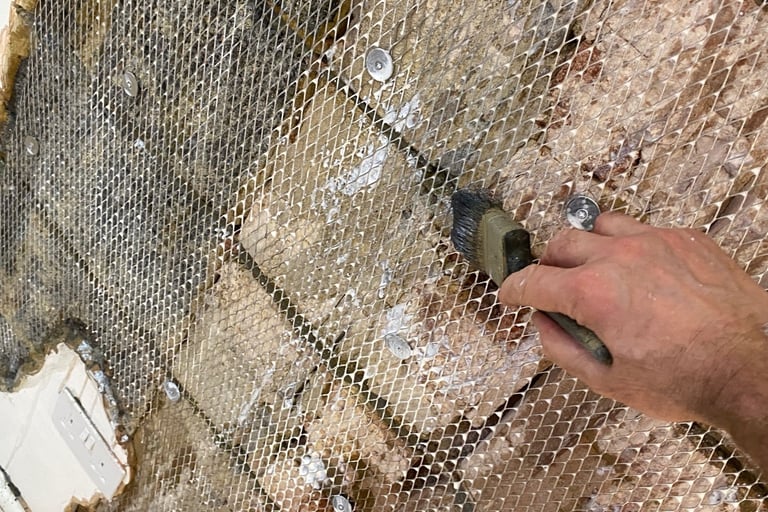 Hand applying bonding agent with a brush onto metal lath mesh for a masonry wall repair.