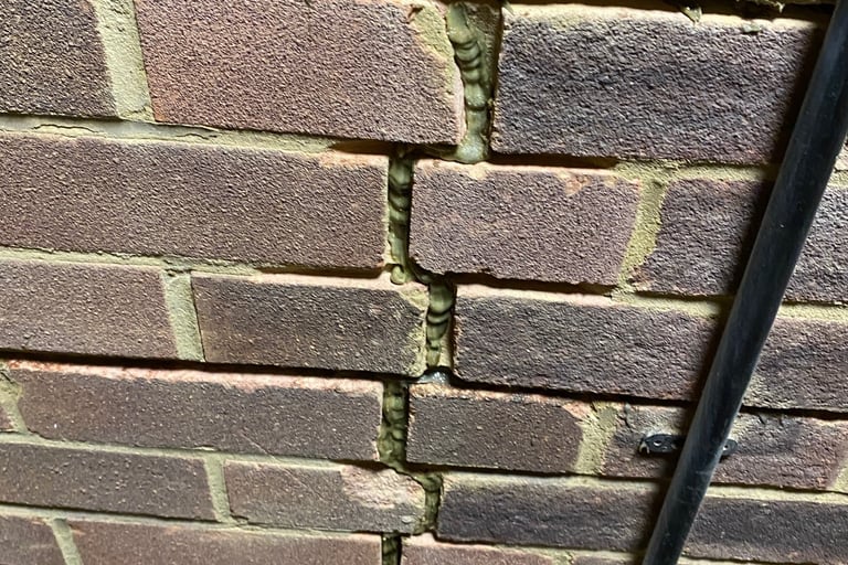 Vertical crack in a residential brick wall showing structural damage and signs of old mortar repair.