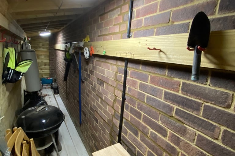 Organized garden stoe orage shed with wall-mounted tool racks, hand trowel, and kettlen brick walls.