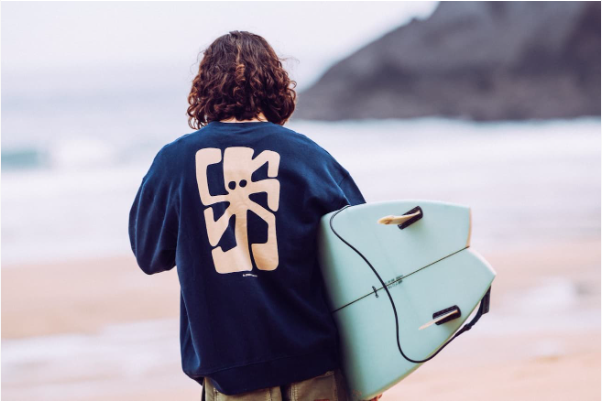 a man with a surfboard on a beach and jonsenisland sweatshirt