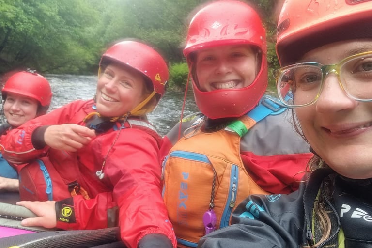 4 women perched on a rock in the middle of the river in white water kayaks. 
