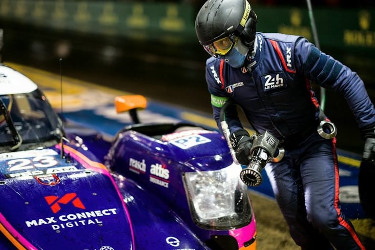 A 24 Hours of Le Mans pit crew member in gear refueling a purple endurance race car during a night pit stop.