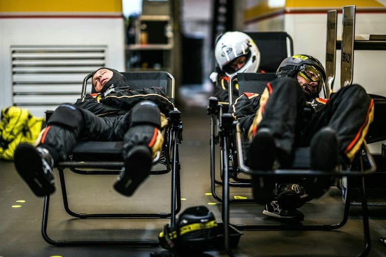 Professional racing pit crew members taking a nap in reclining chairs inside a garage.