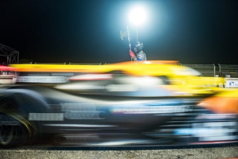 Blurred yellow and black race car speeding past a track official during a night race.