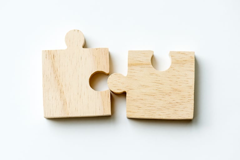 Two wooden puzzle pieces connecting together on a white background, representing teamwork and strategy.