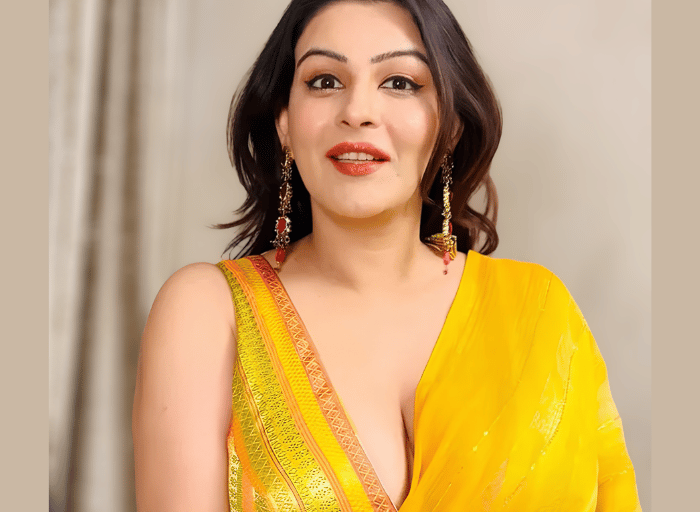 A woman in a vibrant yellow silk saree with gold borders and matching jewelry posing for a portrait.