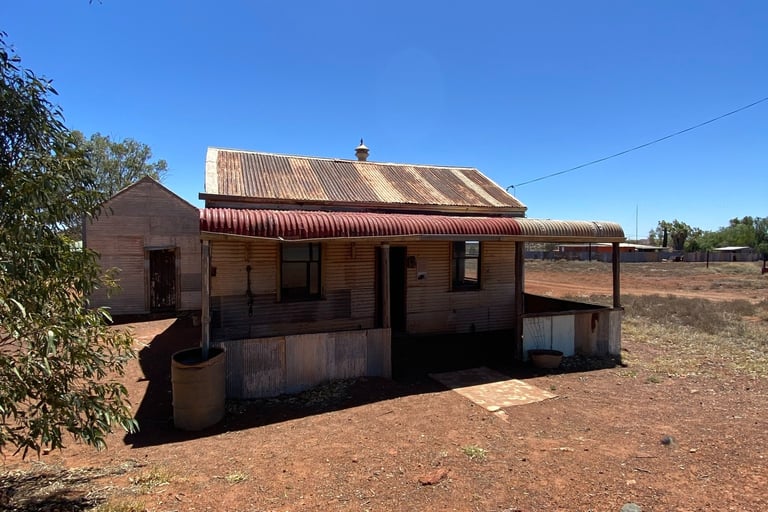Rustic corrugated iron shack in the Australian outback under a clear blue sky.