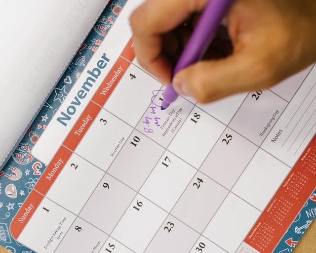 a person holding a pen and writing on a calendar
