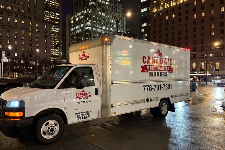 Canada’s Most Wanted Movers box truck operating in downtown Vancouver on a rainy evening.