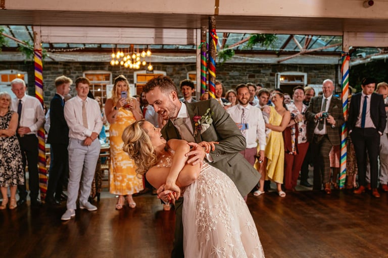 First dance dip at Plas Dinam Country House, the couple beaming as guests cheer them on in the vibrant reception hall.