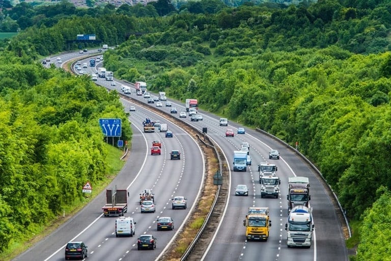 Aerial view of cars and trucks driving on the busy M25 motorway through lush green English countryside.