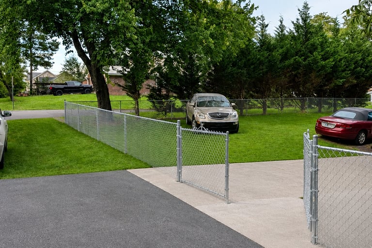 Galvanized silver chain link fence installed along a residential driveway and green lawn.