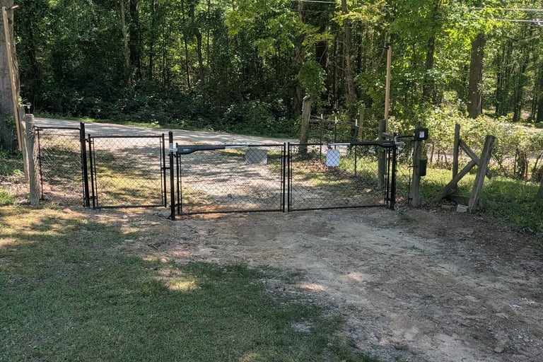 Automatic black chain link driveway gate with electric opener installed on a dirt road entrance.