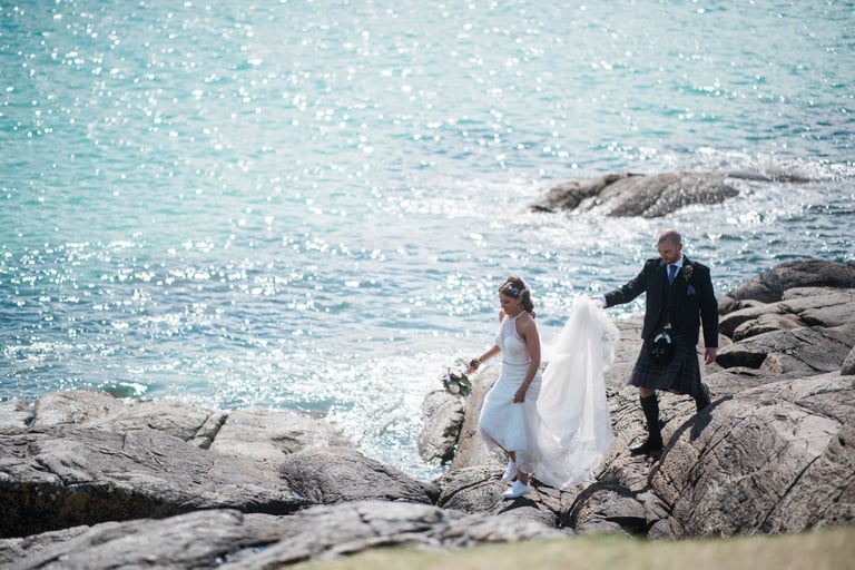 a bride and groom walking down a rocky beach
