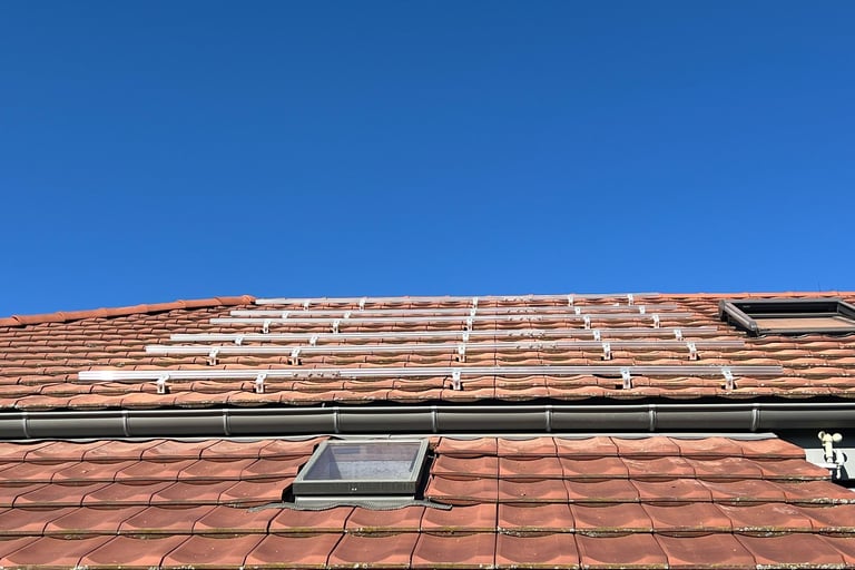 installation des rails de fixation pour panneaux photovoltaïques autour d'un velux sur toiture en tuiles