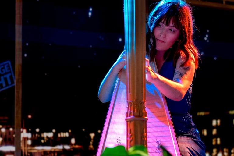 A harpist performing under colorful lights with a city nightscape in the background.