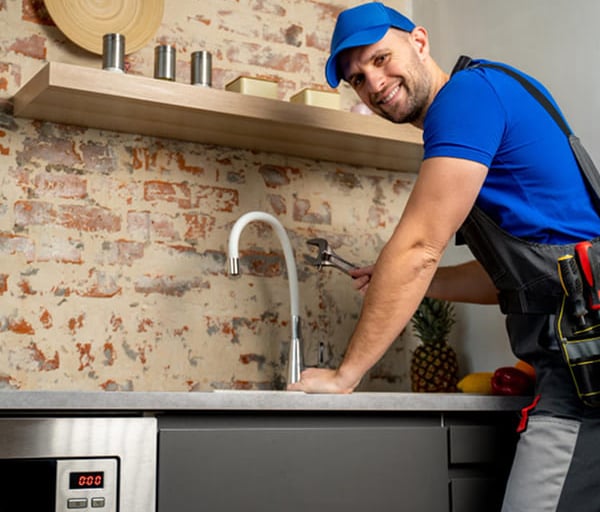 Plombier souriant utilisant une clé pour réparer un robinet de cuisine et inspecter prévenir urgence