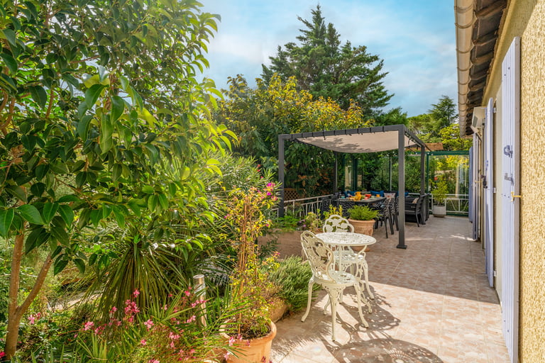 La terrasse ombragée au sud, avec espace repas et coin détente, vue sur le jardin paysager