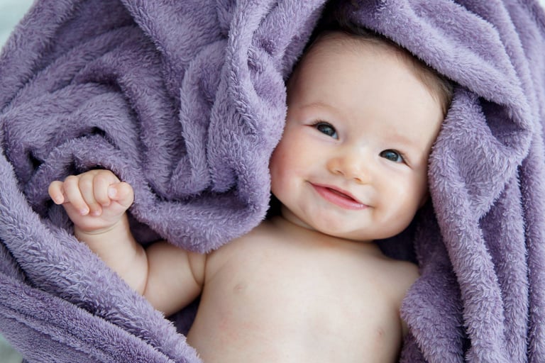portrait de nouveau né, le bébé est souriant et enveloppé dans un tissu violet
