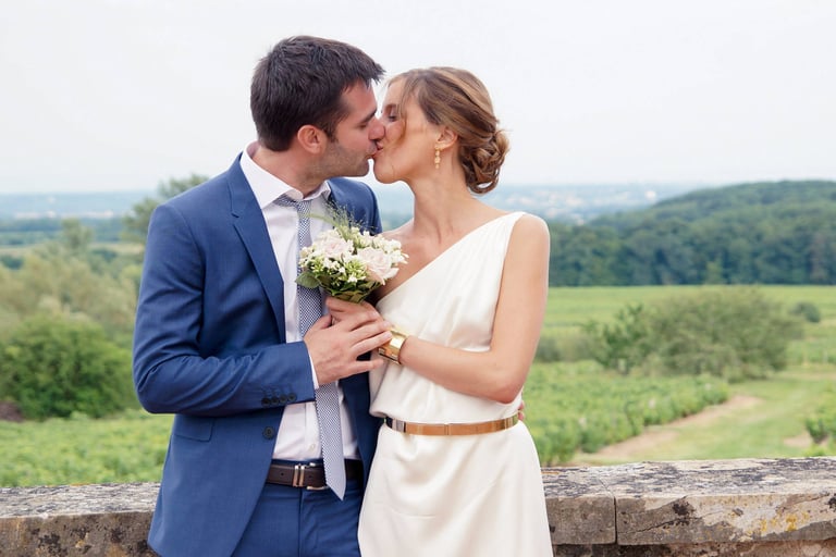 Couple de jeunes mariés qui s'embrasse en tenant leur bouquet de mariage à Dijon.