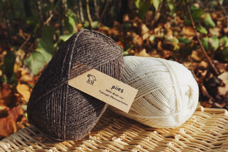 zwei Wollknäuel der Marke piies, einmal hell und einmal dunkel