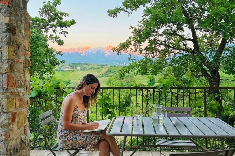 A woman journaling on a balcony with a view to Italian mountains