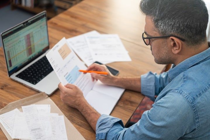 Man working diligently on paperwork, surrounded by a laptop,  and documents.