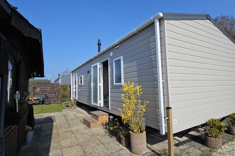 Modern grey mobile home with white trim and a stone patio under a clear blue sky.