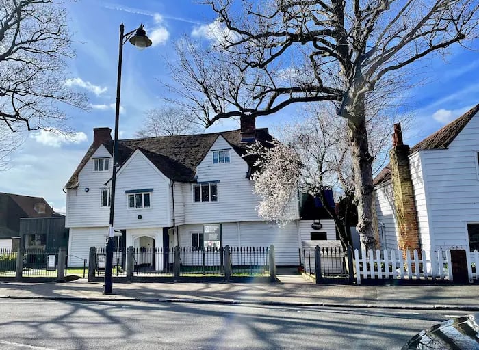 A historic white weatherboard building with gables under bare trees and a blue sky.