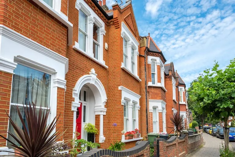 Rows of Victorian red brick terraced houses on a suburban London street under a blue sky.